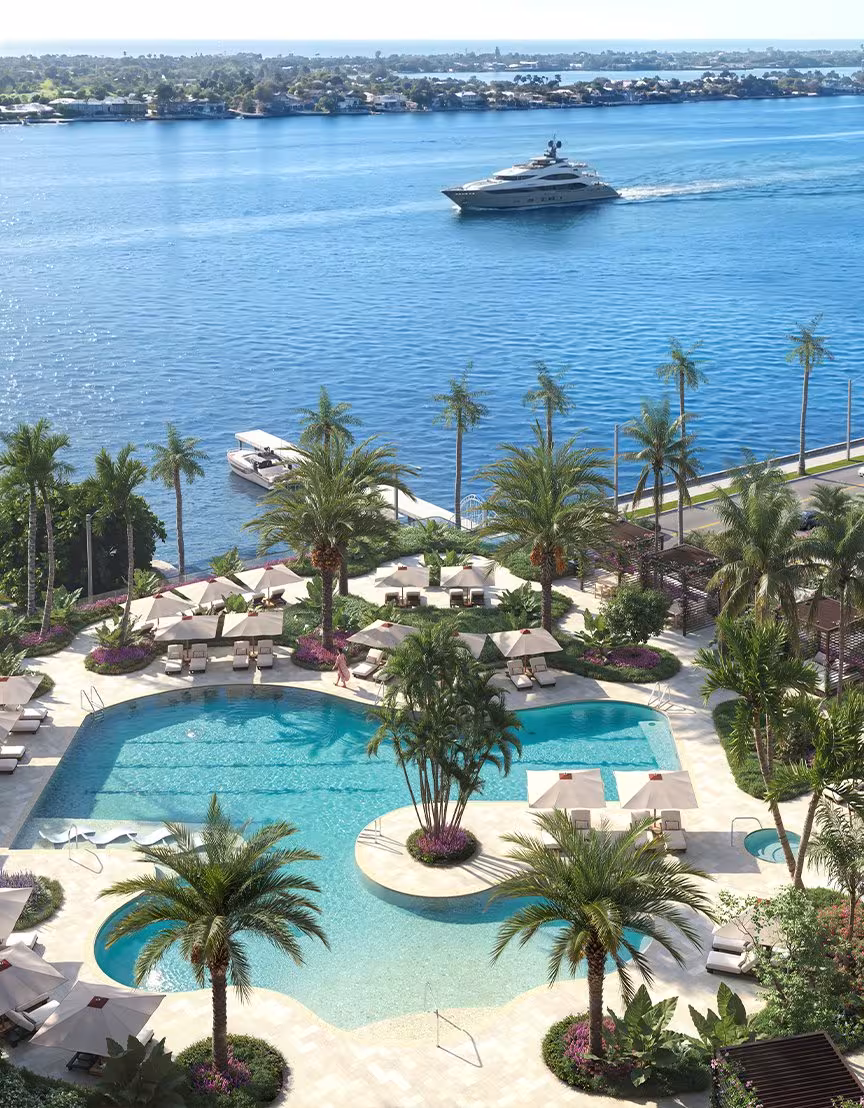 The waterfront pool terrace from above, with a yacht passing on the water beyond